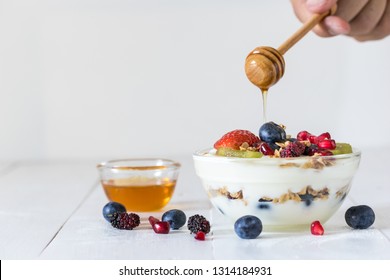 Plain yogurt with strawberry, blueberries, kiwi, granola, pomegranate in a glass bowl and honey on white wooden texture, healthy food and plant-based food concept - Powered by Shutterstock