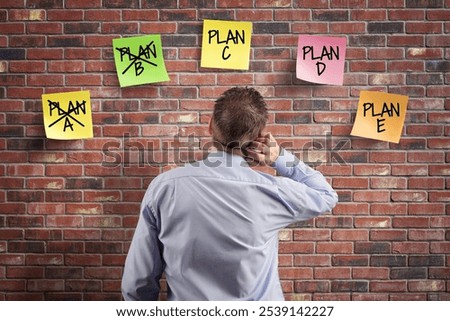 Plan A B C D and E alternative strategy planning and contingency solution, choice and decisions businessman thinking with plan options written on adhesive notes stuck to a brick wall
