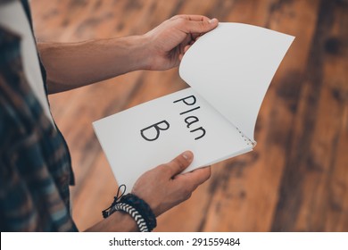 Plan B. Top view of man turning the page of his note pad while standing on the wooden floor 