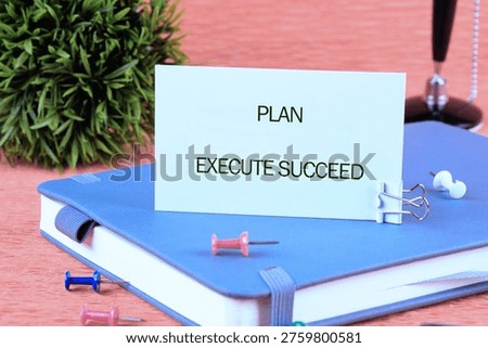 PLAN EXECUTE SUCCEED card on blue journal, with pushpins and a green plant. Focused workspace ready for action.