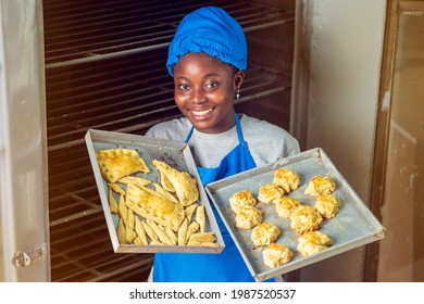 Plan View Of Cheerful African Lady In Apron And Head Wrap, Black Woman Carrying Baked Food In Both Hands 