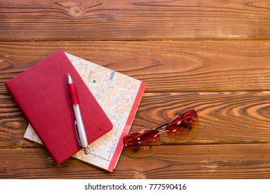 Plan Your Vacation. A A Folded Map, A Red Notebook, A Pen And Sunglasses On A Rustic Wooden Background. Space For A Text Or Product Display, Top View.