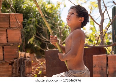 Planaltina, Goias, Brazil-July 25 2020: A Poor Little Boy Playing With A Bamboo Pole Outside His Home In The Impoverished Community Planaltina 