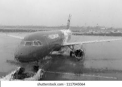 Plane before flight through blurred window with raindrops. Plane black and white. Avaition concept. Travel and transport background. Rainy day in airport. 