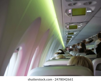 Plane cabin with people sitting stewardesses in background. Great for aviation and travel content. Plane interior featuring passengers and crew, providing a glimpse into in-flight plane experience. - Powered by Shutterstock