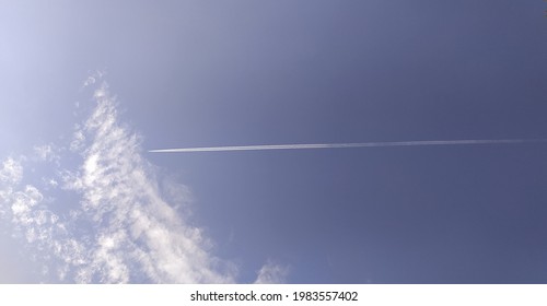 plane crosses horizontally leaving behind a long smoke trail trace. Stunning view of a jet or airplane forming contrails on a clear blue sky background with white clouds. beautiful bottom view.
