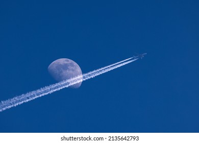 Plane flies pass over the moon on blue sky airplane trail - Powered by Shutterstock