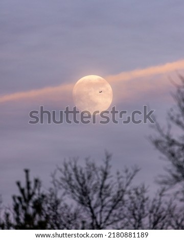 Plane flying across a full moon with soft ethereal sunset light illuminating high level clouds. Long Island New York