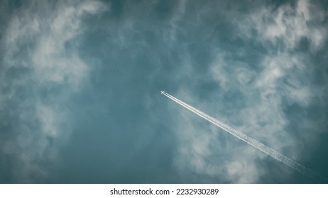 Plane flying high in the sky leaving behind a long trail trace. Stunning view of a jet or airplane forming contrails on a blue sky background with white clouds. - Shutterstock ID 2232930289