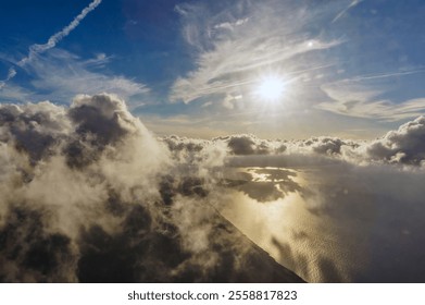 A plane is flying through a cloudy sky with the sun shining through the clouds. The sun is reflecting off the water below, creating a beautiful and serene scene
