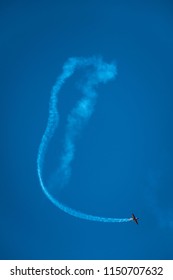 A plane making an acrobatic flight making a loop with white smoke in a blue sky. Concept of aviation show performance