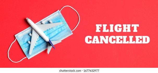 Plane model and face mask on a red background with text flight cancelled. Flight cancellation due to the impact of coronavirus (COVID-19) concept.