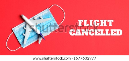 Plane model and face mask on a red background with text flight cancelled. Flight cancellation due to the impact of coronavirus (COVID-19) concept.