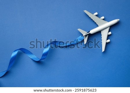 Plane model and ribbon as flight path on blue background, top view
