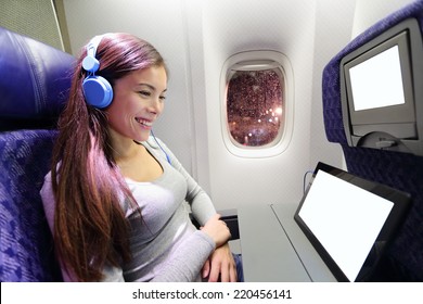 Plane Passenger In Airplane Using Tablet Computer. Woman In Plane Cabin Using Smart Device Listening To Music On Headphones.