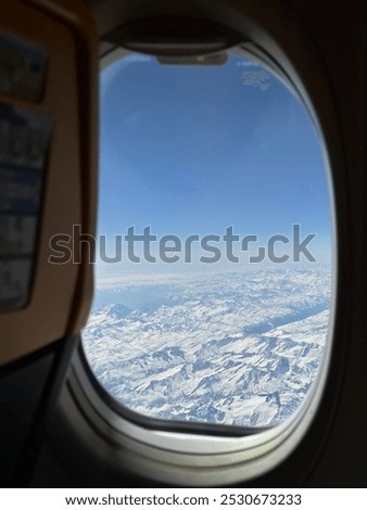 Plane view from the plane window to the snowed mountains and blue sky 