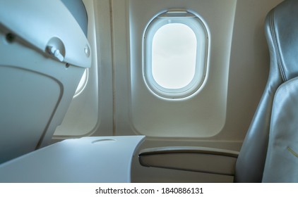 Plane window with white sunlight. Empty plastic airplane tray table at seat back. Economy class airplane window. Inside of commercial airline. Seat with armchair. Leather seat of economy class plane.