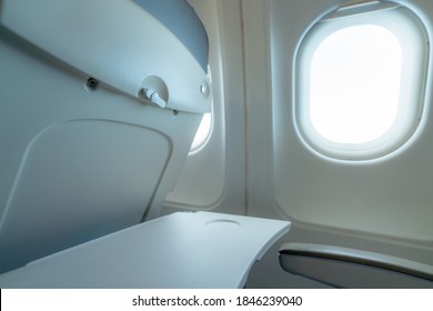 Plane Window With White Sunlight. Empty Plastic Airplane Tray Table At Seat Back. Economy Class Airplane Window. Inside Of Commercial Airline. Seat With Armchair. Leather Seat Of Economy Class Plane.