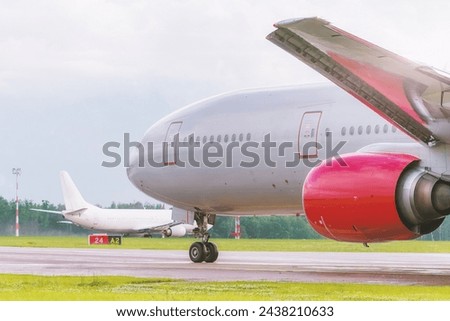 The planes lined up on the taxiway, awaiting clearance from the control tower. The main character of the photo, an airplane with a bright red engine, demonstrates the scale of aircraft technology