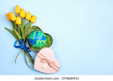 Planet Earth in a heart gift box with a bouquet of yellow tulips on a blue background. Copy space for text. Earth Day, ecology and nature protect. - Powered by Shutterstock