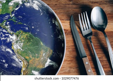 The planet Earth plate with a spoon, fork and knife on a wooden background. World hunger concept. Feed the world. 