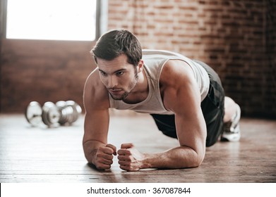 Plank it! Confident muscled young man wearing sport wear and doing plank position while exercising on the floor in loft interior
