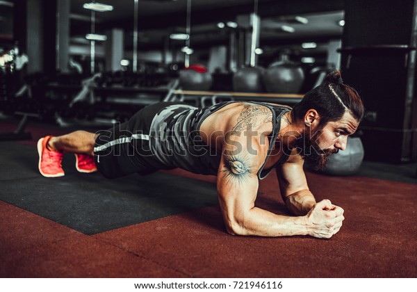 Plank it. Confident\
muscled young man wearing sport wear and doing plank position while\
exercising in gym.