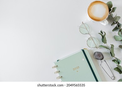 Planner, cup of coffee and milk, eucalyptus leaves, glasses, tea strainer on white background. Flat lay, top view, copy space.