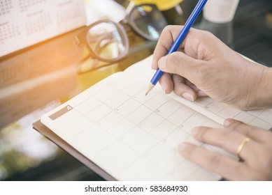 Planner writing daily appointment at Calendar. Woman hand mark and noted schedule (holiday trip) on diary book at home office desk. Calendar reminder event for planner concept.