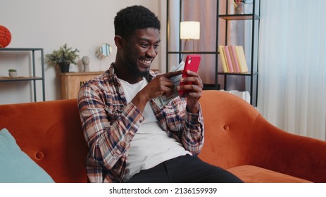 Planning Family Budget. Smiling African American Man Counting Money Cash, Use Mobile Phone Calculate Domestic Bills At Home. Joyful Guy Satisfied Of Income And Saves Money For Planned Vacation, Gifts