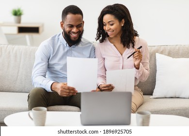 Planning Family Budget. Smiling Black Couple Holding Papers, Calculating Domestic Bills And Checking Household Expenses, Reading Documents Or Receipt From Bank, Talking About Investment And Finance