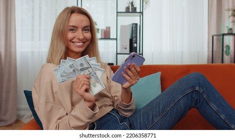 Planning Family Budget. Smiling Caucasian Girl Counting Money Cash, Use Smartphone Calculate Domestic Bills At Home. Joyful Young Woman Satisfied Of Income And Saves Money For Planned Vacation, Gifts