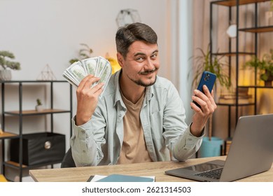 Planificación del presupuesto familiar. Hombre caucásico sonriente que cuenta el dinero en efectivo del dólar usa el teléfono inteligente para calcular las facturas nacionales. El tipo satisfecho de los ingresos, ahorra dinero del salario en el lugar de trabajo de la mesa de la oficina en el hogar. Estilo de vida