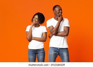 Planning Future Together. Young African-american Couple Day Dreaming On Orange Studio Background. Pensive Black Man And Woman Standing Next To Each Other And Thinking, Touching Their Chins