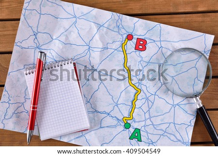 Planning a path on a sheet of paper on a wooden table. With pen notepad and magnifying glass. Top view