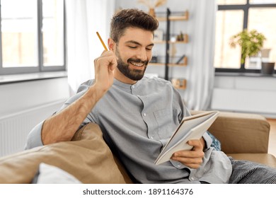 planning and people concept - happy smiling man with to notebook and pencil at home