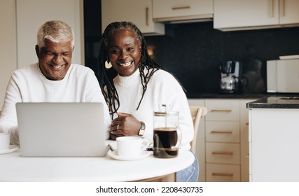 Planning For Retirement Together. Carefree Senior Couple Smiling Cheerfully While Using A Laptop. Happy Mature Couple Researching Their Retirement Options At Home.