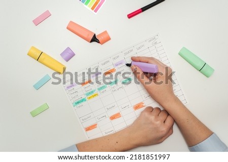 Planning the school year. Drawing up a student schedule. The girl makes edits with a purple marker in the planner on the white table. Multicolored markers and stickers on a white table.