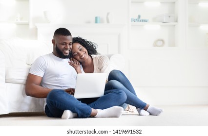 Planning summer vacation. Cute african american couple searching hotel and resort online, using laptop on floor at home, free space