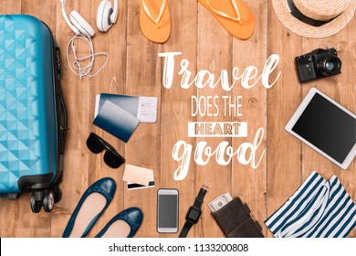 Planning for trip set of travel accessories on wooden floor. Travel background with luggage, shoes, passports, flip flops, hat, camera. "Travel does the heart good" - lettering