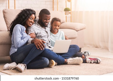 Planning vacation together. African father, mother and daughter using laptop at home, sitting on floor, copy space - Powered by Shutterstock