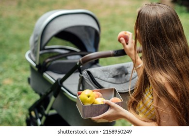 Plans And Diet For Breastfeeding Moms. Allergy In An Infant Child During Breastfeeding The Baby. Young Mom Eating Fruits While Walk With Newborn Baby In Stroller.