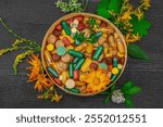 Plant based supplements, natural vitamins with fresh herbs and flowers. Organic ingredients medication suggesting holistic health concepts, alternative lifestyle. Dark wooden background, top view