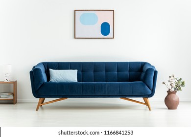 Plant next to blue settee with cushion in white minimal living room interior with poster. Real photo - Shutterstock ID 1166841253