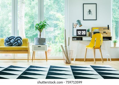 Plant on white cabinet next to yellow settee with blue pillow in bright workspace with yellow chair