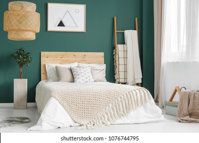 Plant And Rattan Lamp In Green Cozy Bedroom Interior With Wooden Bed Against The Wall With Poster