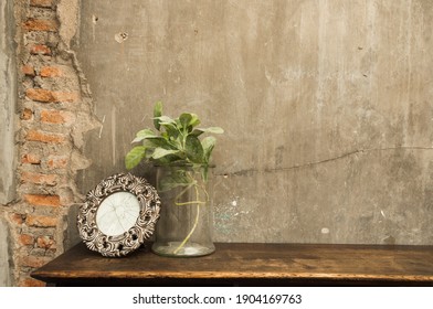 Plant In A Vase On The Wooden Table With Broken Picture Frame , Gray Concrete Wall