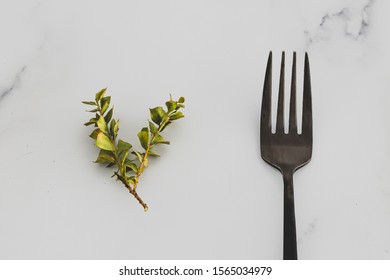 Plant-based Diet Conceptual Still-life, Small Branch Of Green Leaves Next To Black Fork On Marble Table