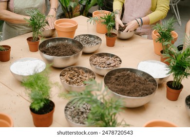 Planting house plants two women wearing striped aprons.  table with soil, bowls, root balls, Perlite and plants. Top view and unrecognizable people - Powered by Shutterstock