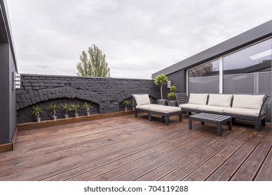 Plants and beige garden furniture on terrace with wooden floor and black brick wall